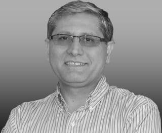 Black and white headshot of a smiling man wearing glasses and a striped button-down shirt.