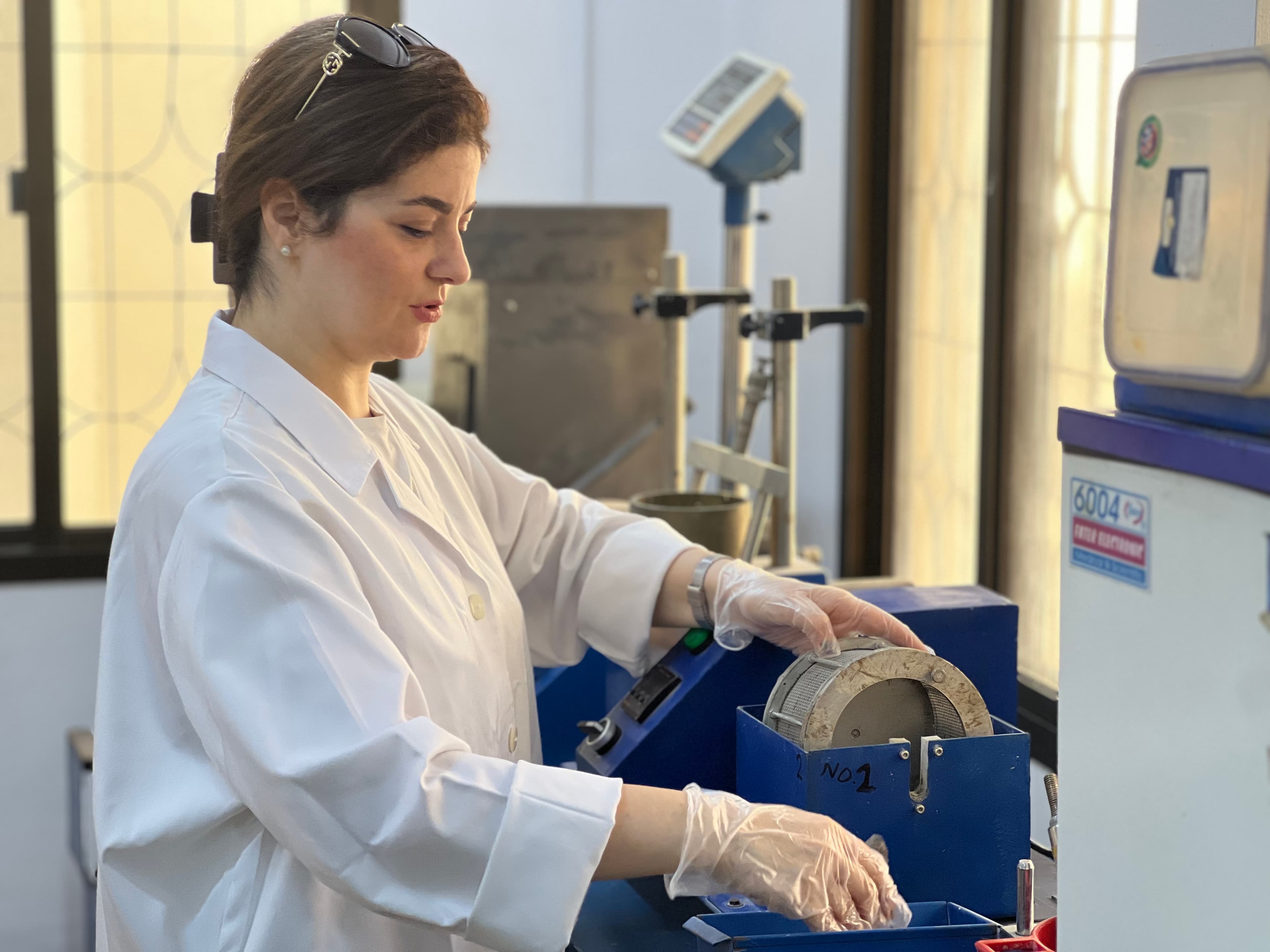 Female scientist in a white lab coat and gloves using specialized machinery in a laboratory.