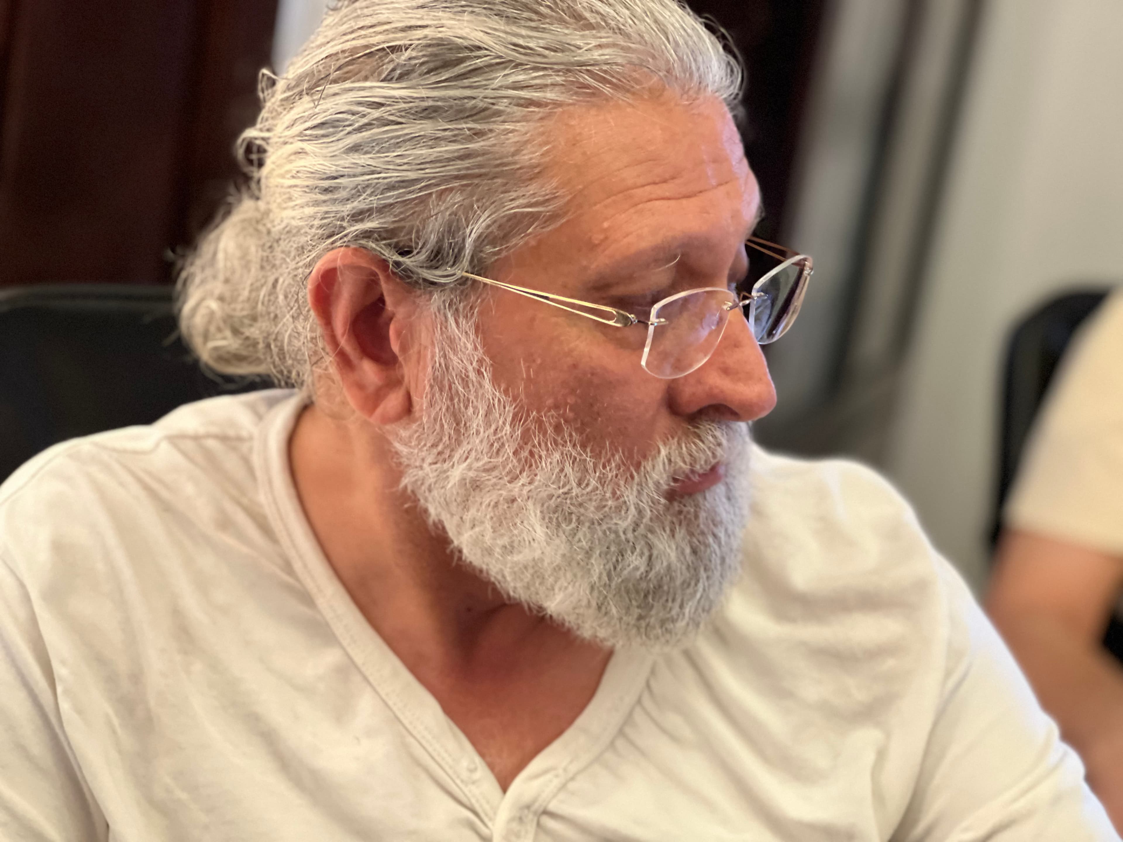 Side profile of a man with grey hair in a bun, white beard, and glasses.